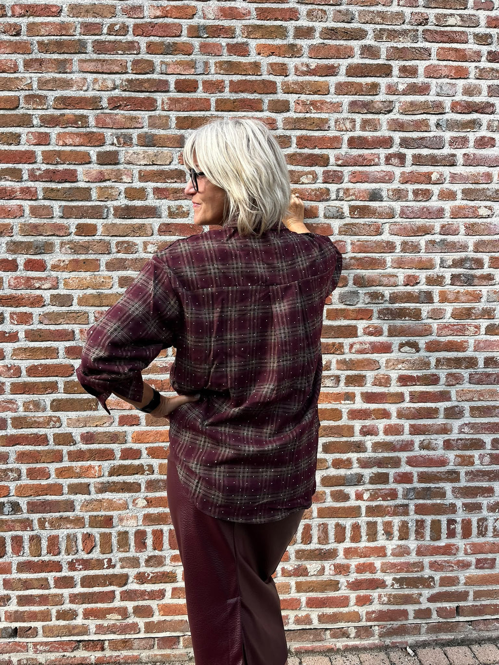 Dit prachtige bordeaux geruite hemd is een echte eyecatcher. Het tijdloze ruitpatroon krijgt een vrouwelijke en feestelijke twist dankzij de subtiele strassdetails, die het hemd net dat beetje extra geven.