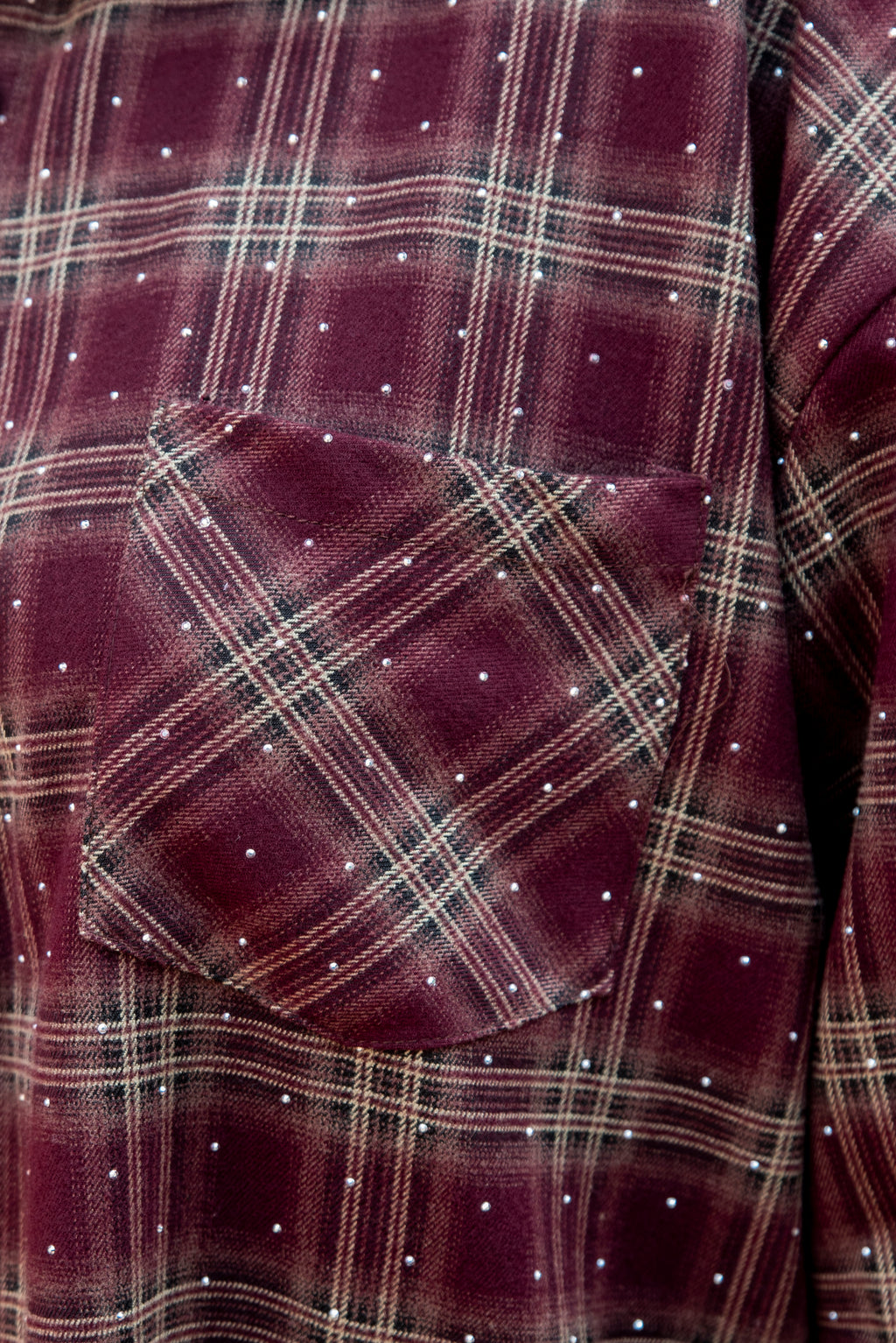 Dit prachtige bordeaux geruite hemd is een echte eyecatcher. Het tijdloze ruitpatroon krijgt een vrouwelijke en feestelijke twist dankzij de subtiele strassdetails, die het hemd net dat beetje extra geven.