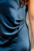 Deze prachtige lange blauwe satijnen jurk valt elegant tot aan de enkels en heeft een mooie, verfijnde halsuitsnijding die de nek en schouders subtiel accentueert.